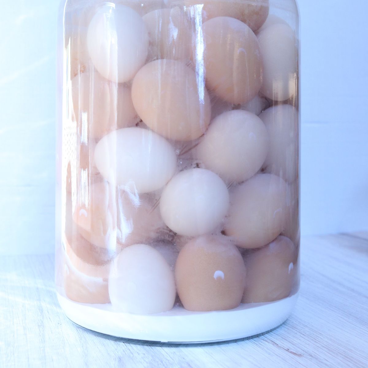 a jar full of brown and tan eggs that have been water glassed using pickling lime. The lime has settled to the bottom of the jar and is visible while sitting on the shelf.