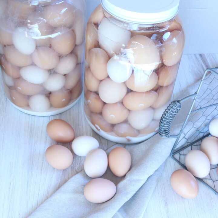 two large jars containing a variety of multi colored eggs that have been water glassed using pickling lime. a handful of farm fresh eggs sits nearby.