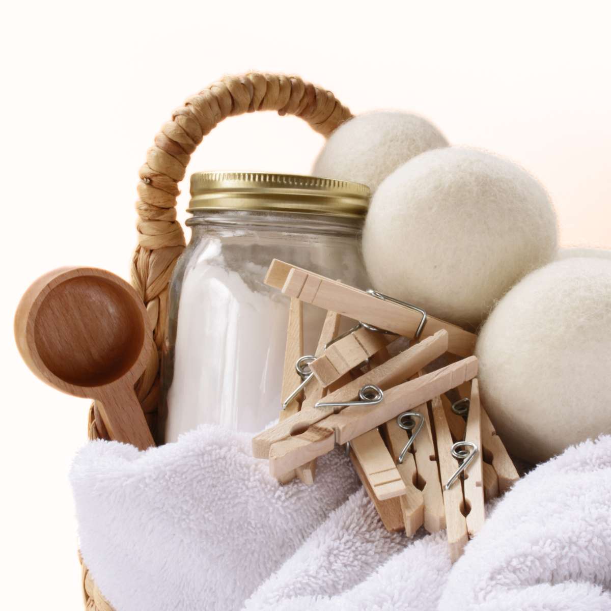 A wicker basket full of clothespins, wool dryer balls and homemade laundry detergent with essential oils.