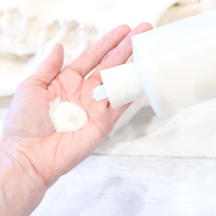 A womans hand holding some white DIY sunscreen alternative cream she just made. Her other hand is holding the clear bottle.