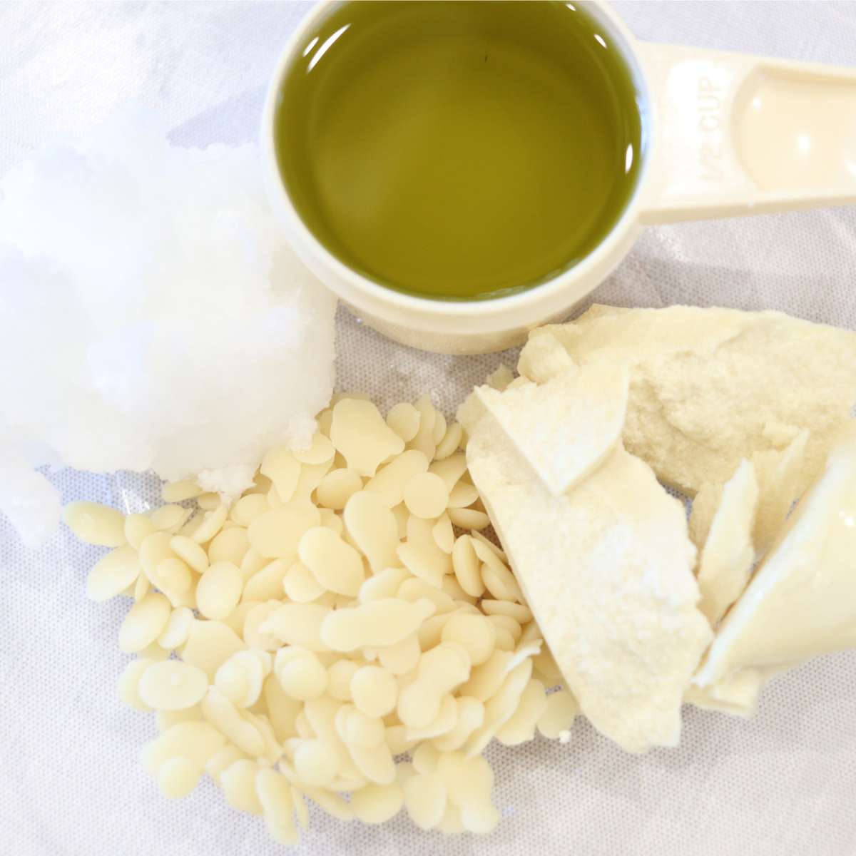 DIY Natural Sunscreen Alternative Ingredients in a clear glass bowl. Beeswax pellets, cocoa butter, and coconut oil.