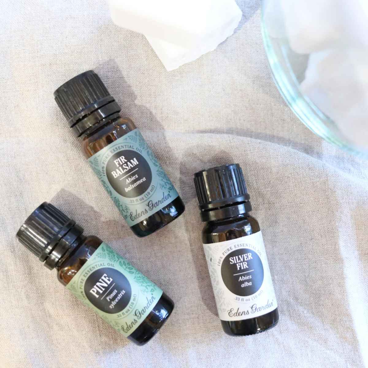 Three small bottles of essential oils being used to make DIY cleaning products. All three oils are tree scented including pine, silver fir and fir balsam.