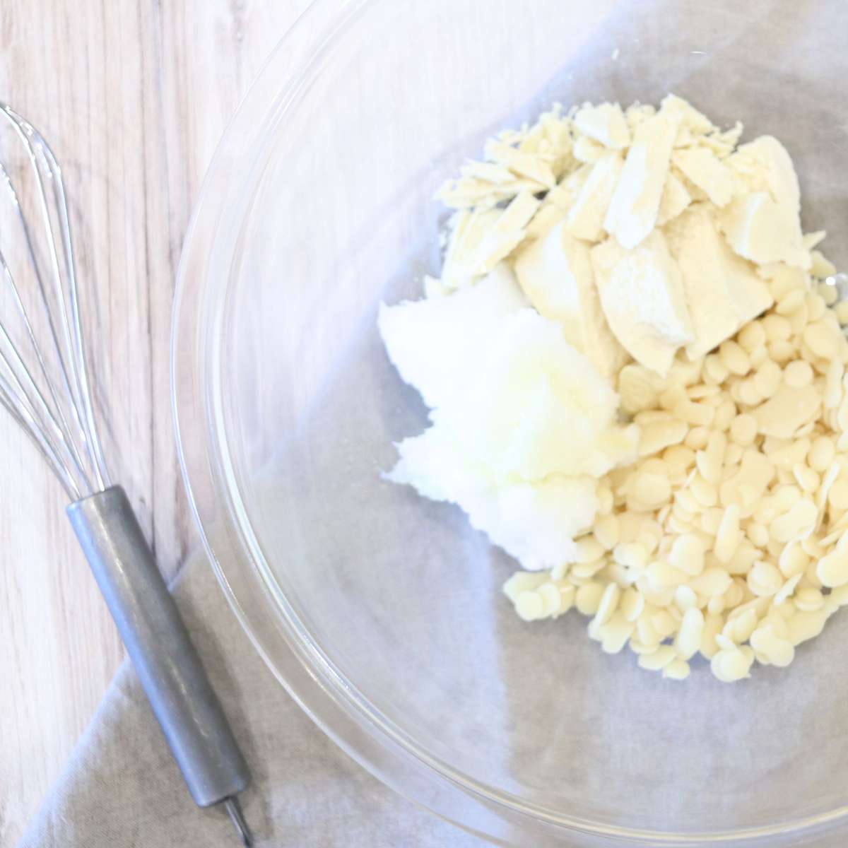 A clear bowl of ingredients that are going to be used to make a natural sunscreen alternative recipe. A silver whisk sits near the side of the bowl.