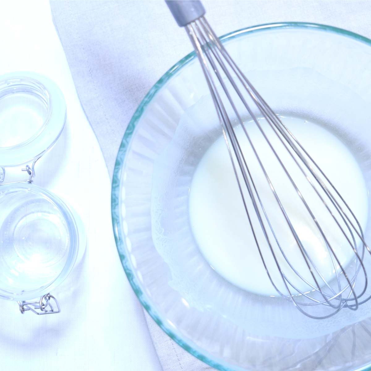 A clear bowl with melted ingredients for homemade natural deodorant. A metal whisk sits in the bowl to whisk ingredients as needed while cooling.