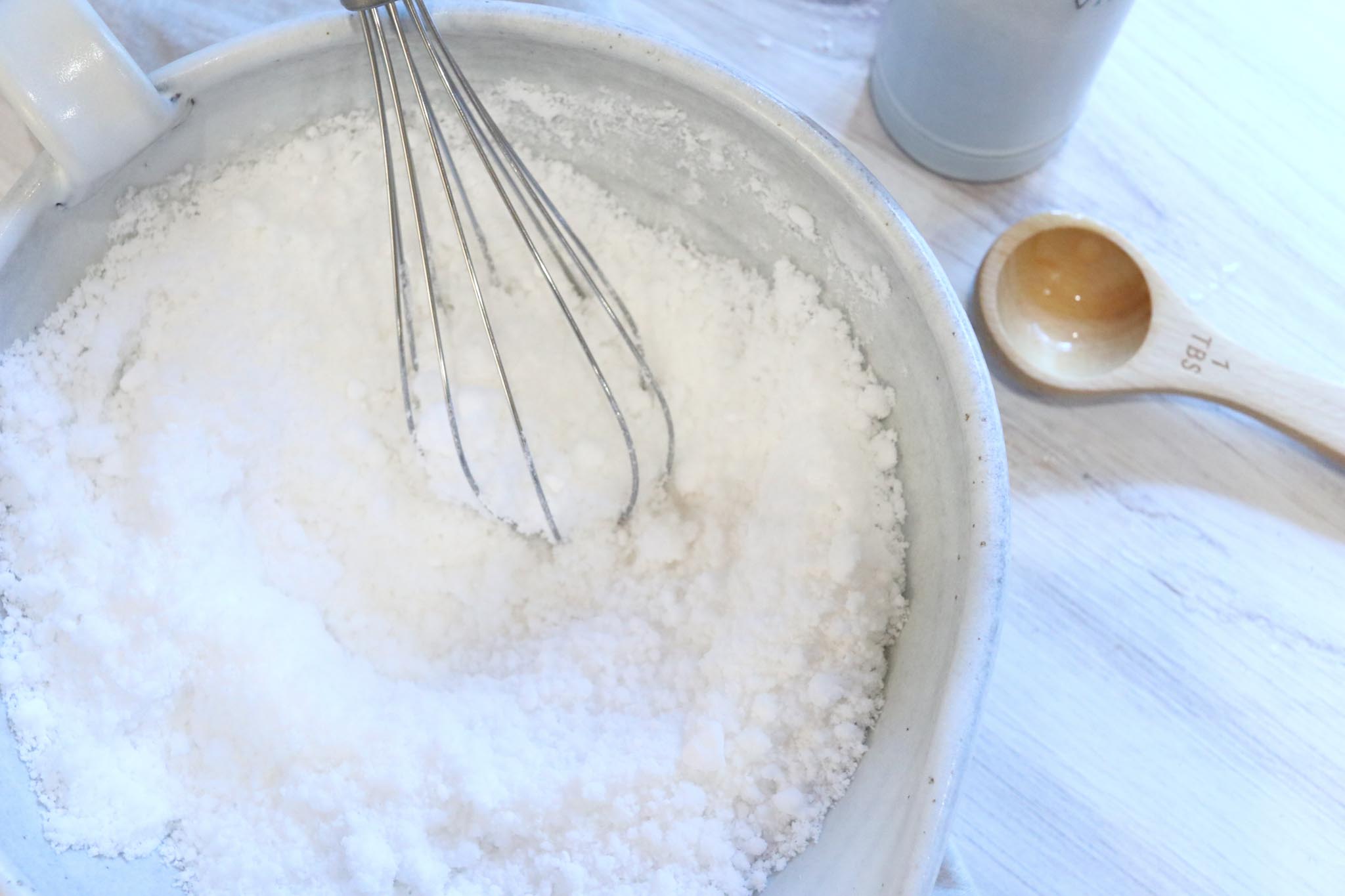 A white bowl with powdered ingredients to make toilet bowl cleaner. A whisk is being used to mix the ingredients together. 