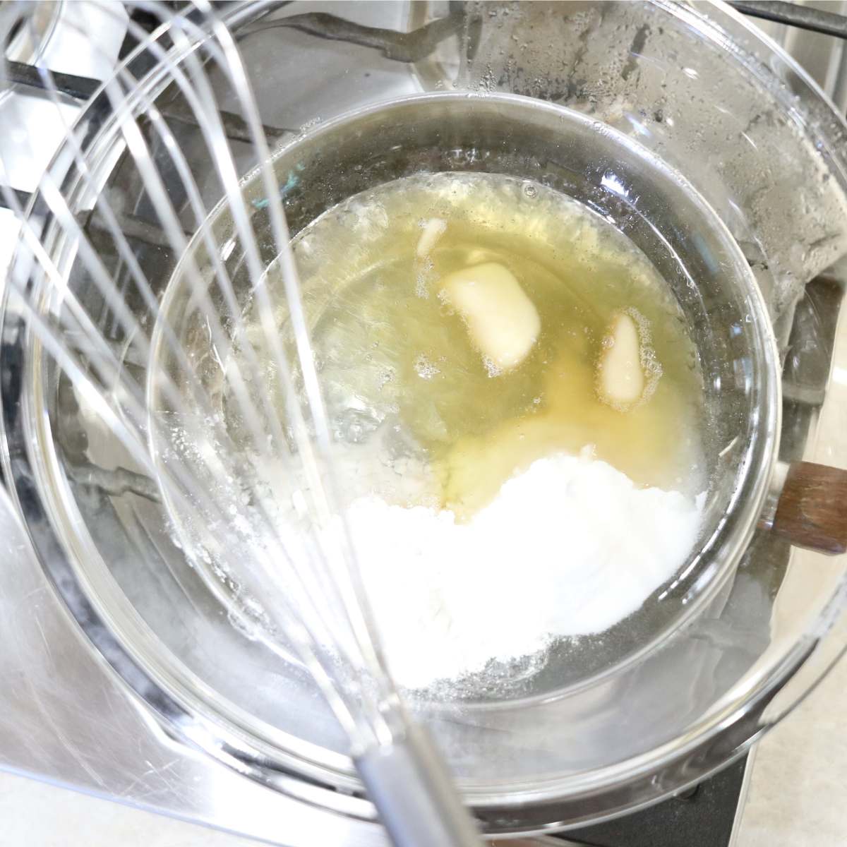 A bowl of homemade deodorant ingredients being melted together using a double broiler pan. A whisk is nearby to stir when needed. The liquid is almost fully melted together.