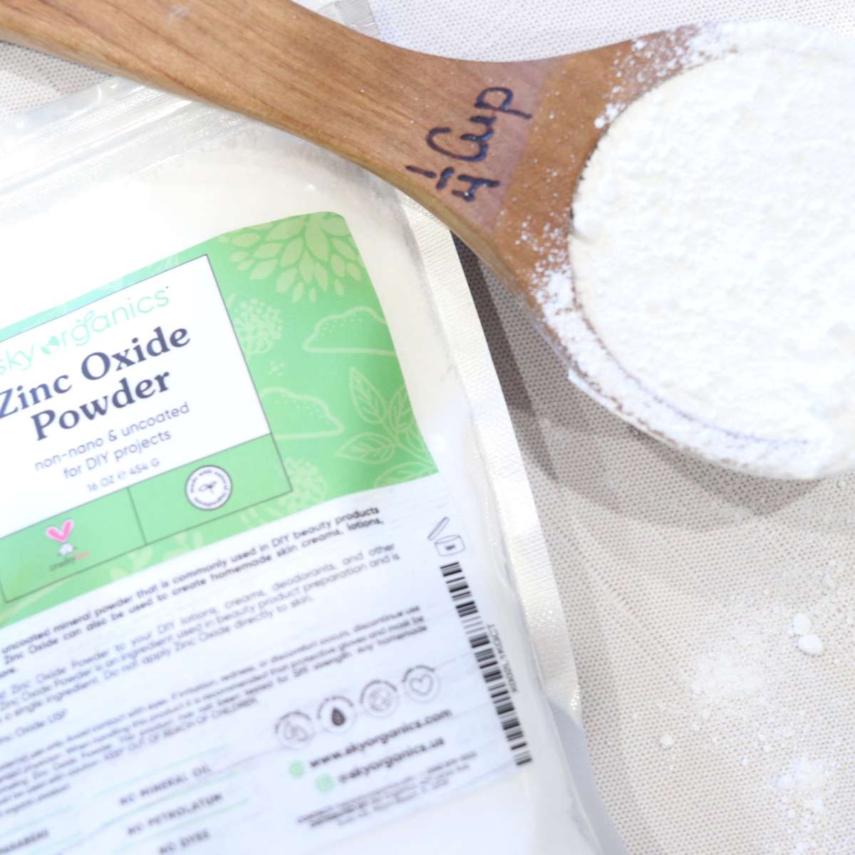 A bag or organic non-nano zinc oxide powder sitting on a table next to a wooden measuring cup.