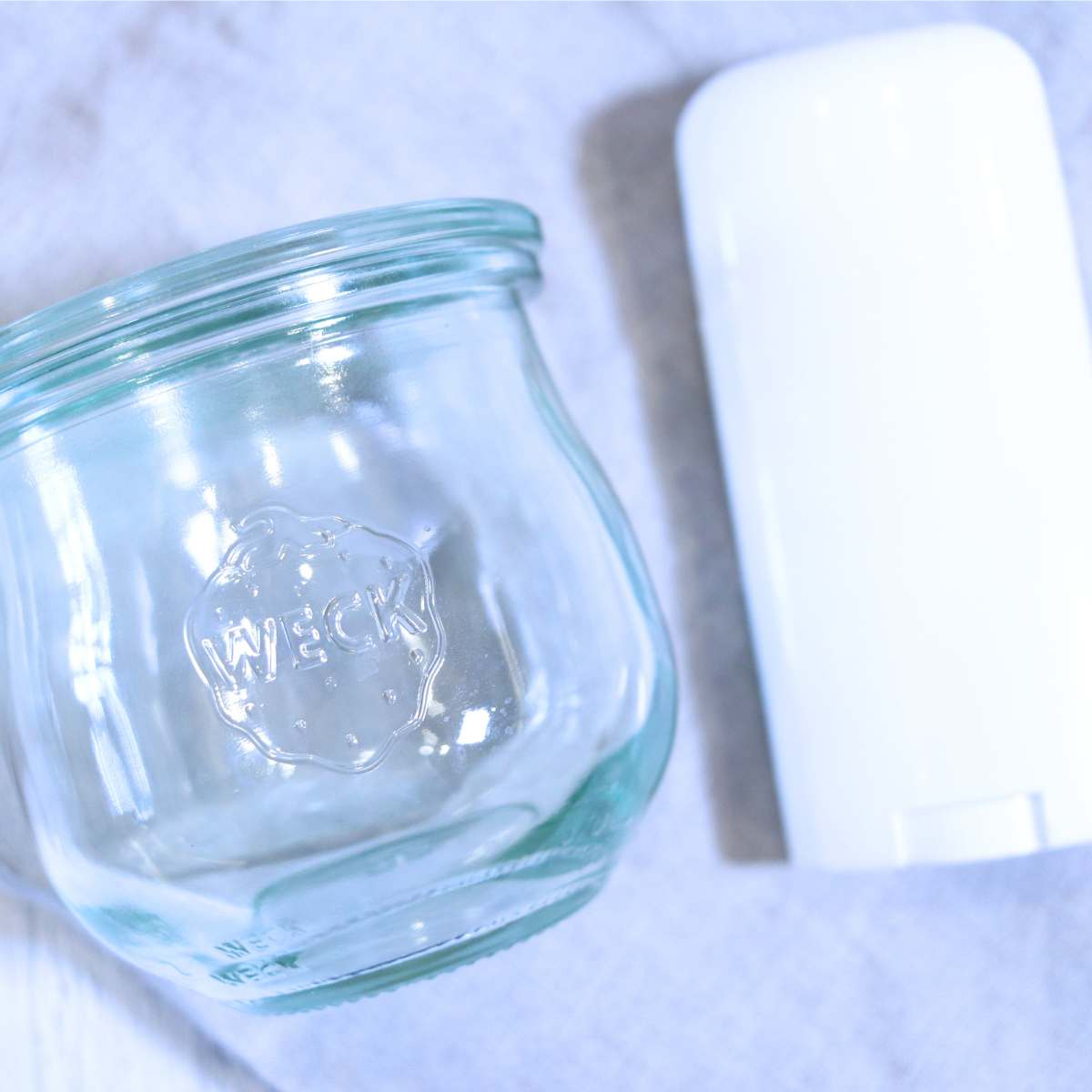 A white plastic empty deodorant container and a clear glass Weck jar used for storing DIY Deodorant.