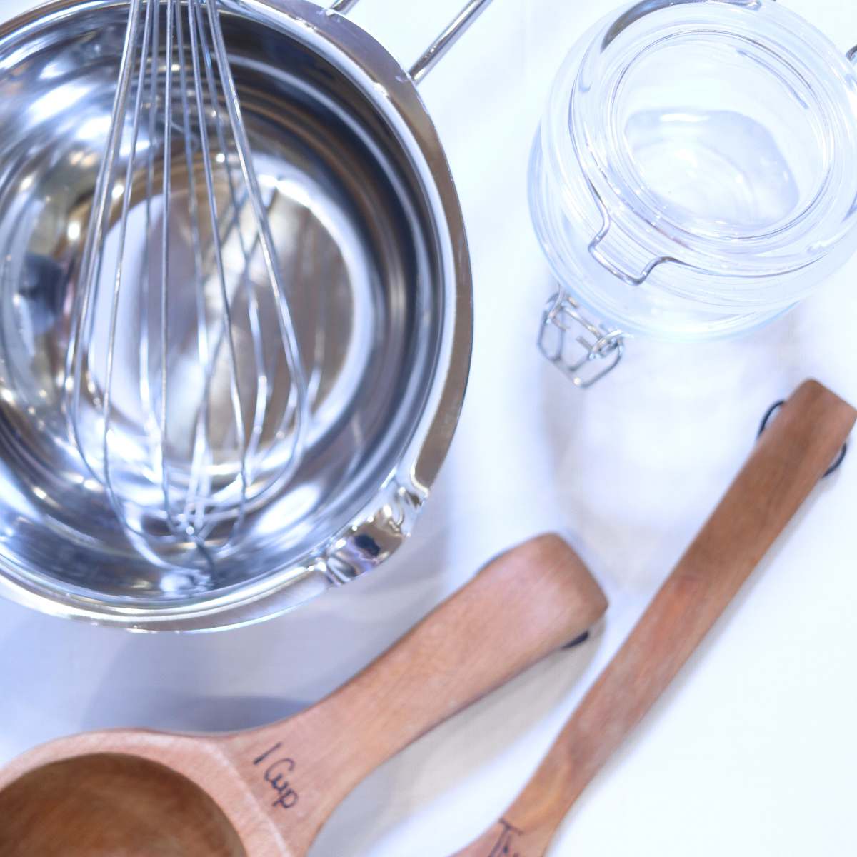 Supplies used for making homemade natural deodorant recipe. A stainless double broiler pot, metal whisk, wooden measuring spoons and a glass jar with a flip top lid to hold DIY Deodorant