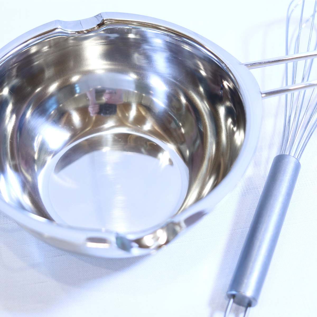 Supplies for homemade natural deodorant without baking soda. A silver metal double boiler pot and metal whisk sitting on a table.