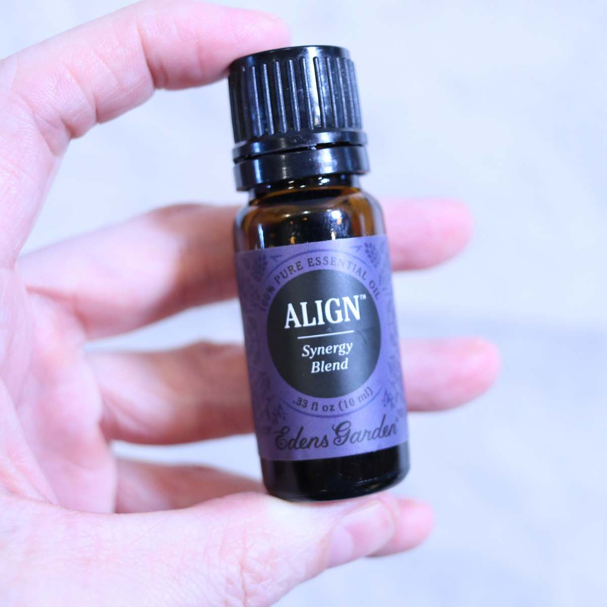 A womans hand is holding an amber bottle of Align essential oil being used for a DIY natural deodorant recipe. The bottle has a dark purple label by Edens Garden Essential Oil brand.