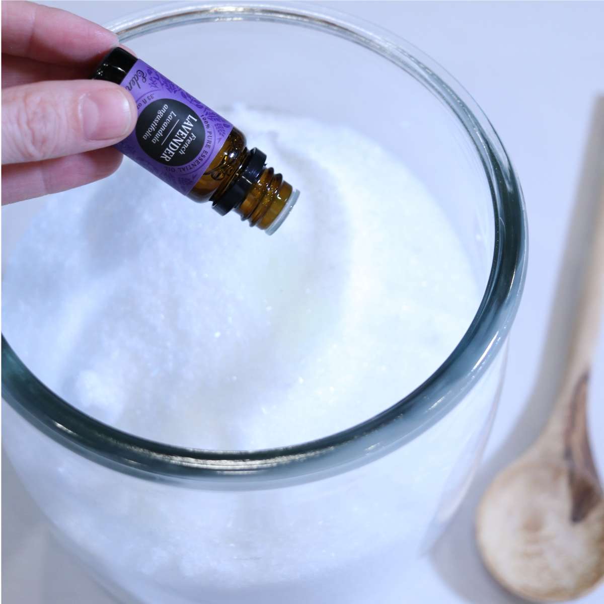 A womans hand is holding a bottle of lavender essential oil and dripping it into her DIY laundry Scent booster powder to add a natural fragrance to her recipe to use in her laundry.