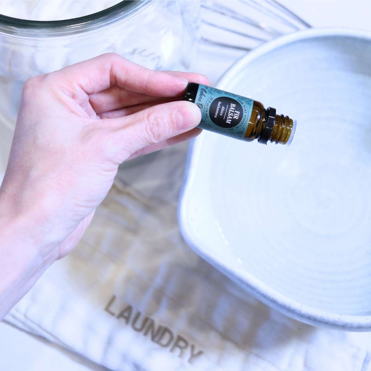 A womans hand is adding essential oils to her DIY dryer sheets to add a natural non-toxic fragrance.