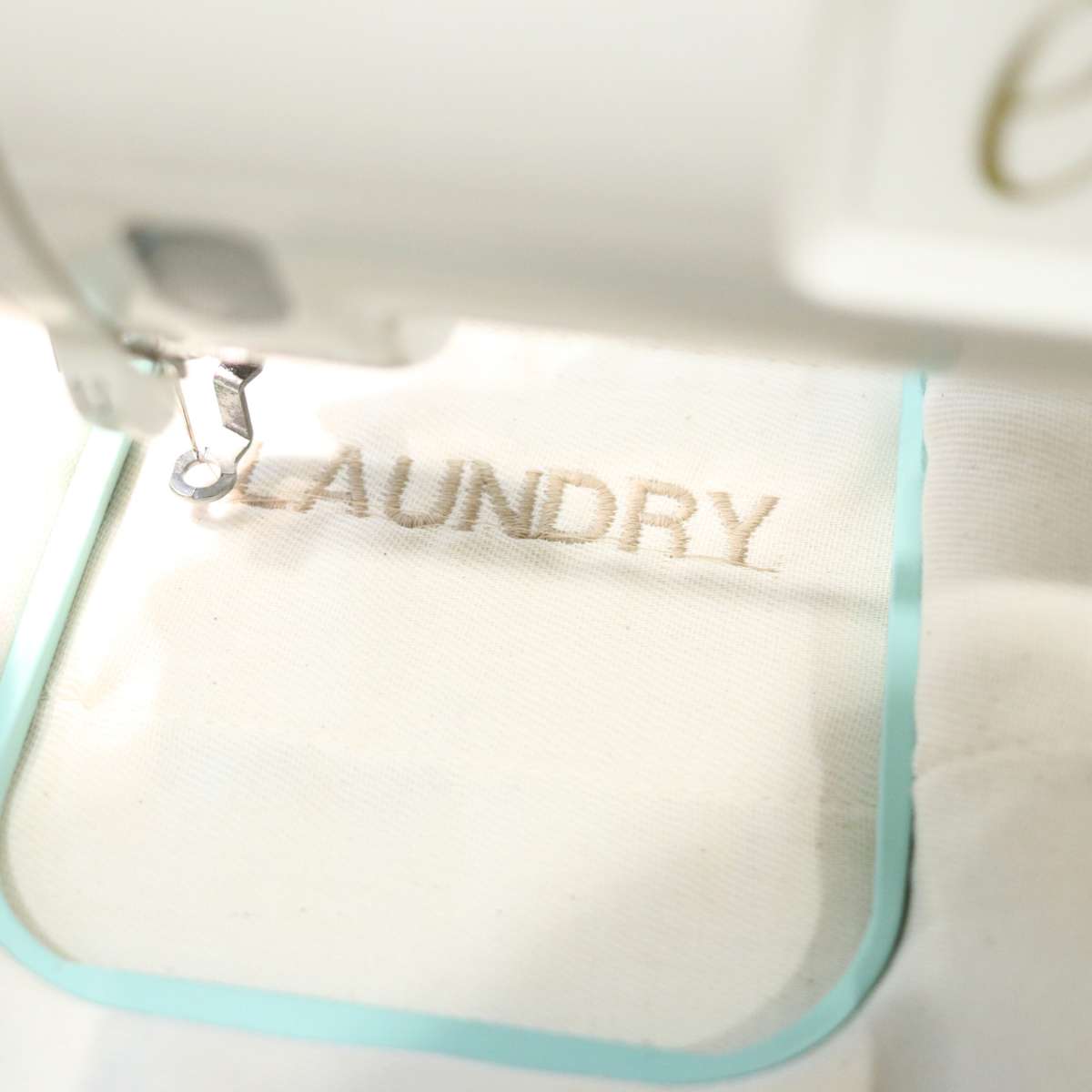 A white embroidery machine is embroidering unbleached flat fold diapers with the word laundry. These flat folds will be used as DIY non-toxic dryer sheets. 