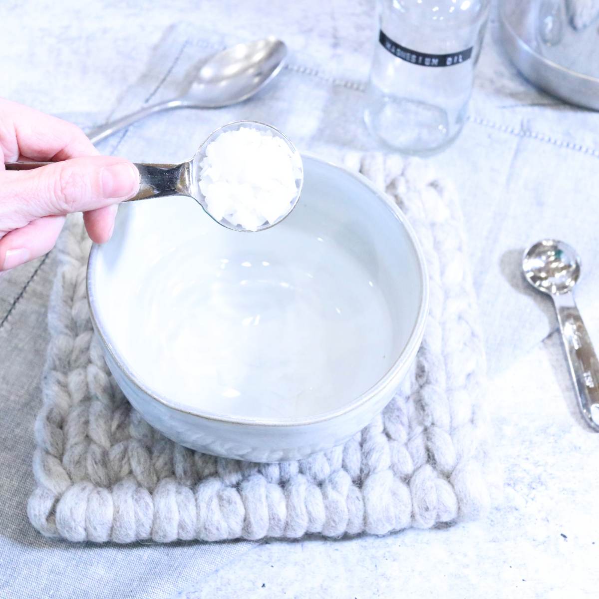 Holding onto a Tablespoon of magnesium flakes, a woman is carefully adding them to a boil of boiling water to make her magnesium oil recipe.