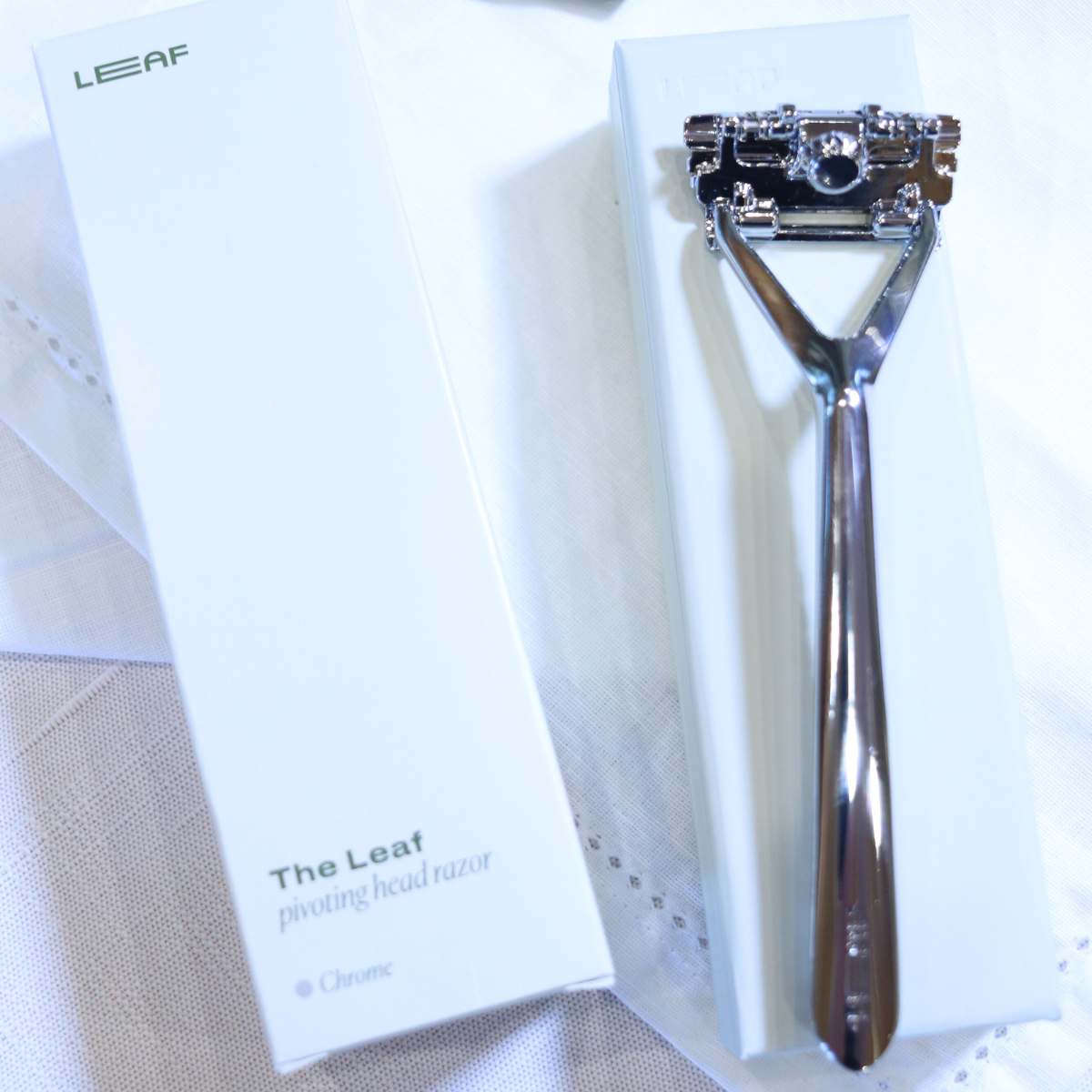 A silver zero waste shave razor sitting next to the white box it comes in. Sitting next to the razor and empty box is a green box or razor blade refills.