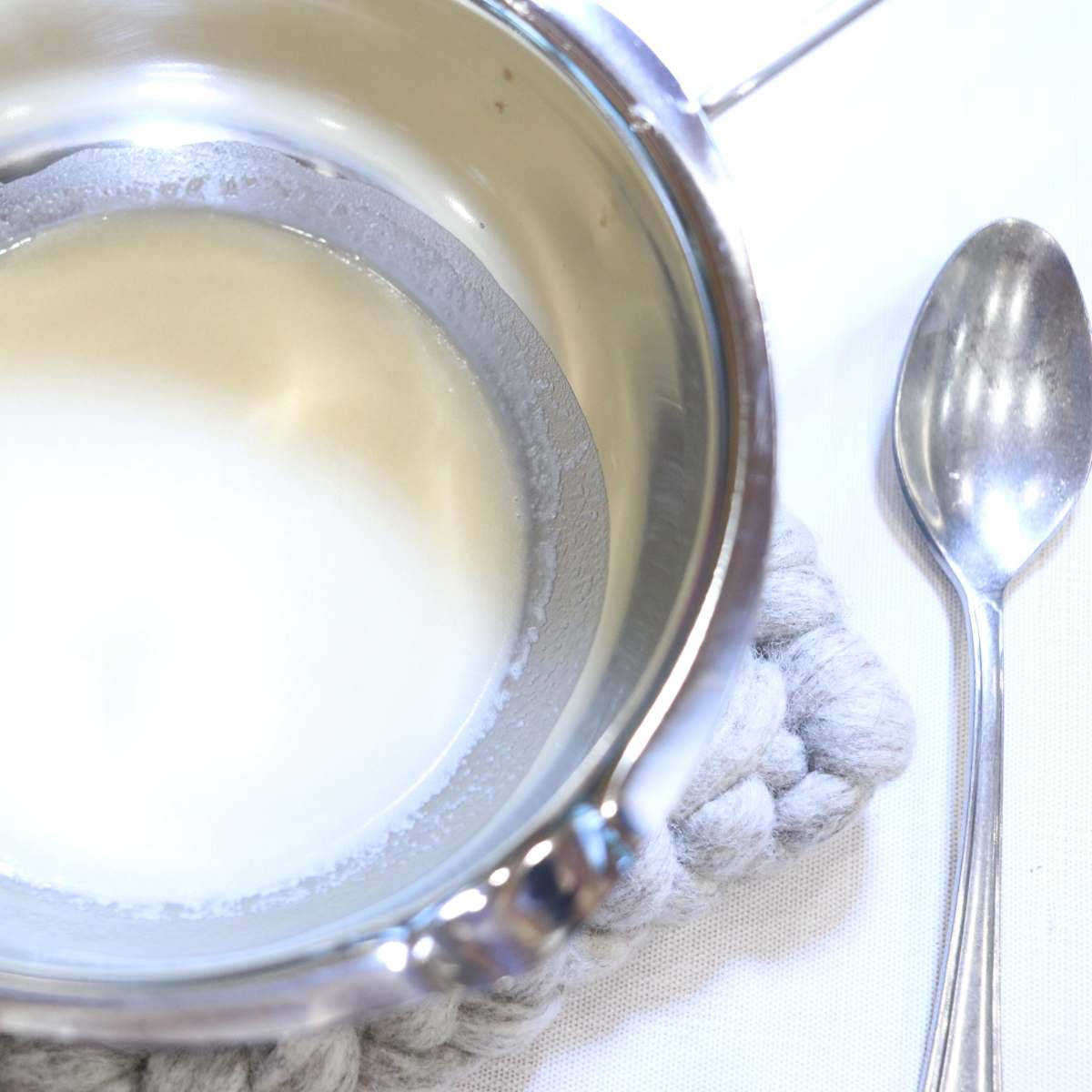 A metal double boiler with melted ingredients for homemade natural deodorant. A silver mixing spoon resting near the pot.