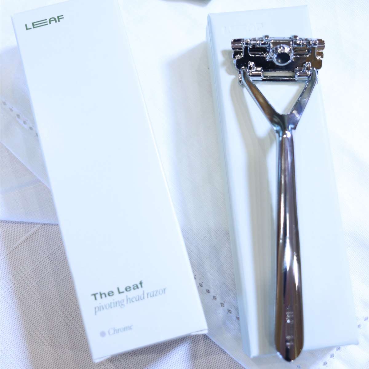 A silver zero waste shaving razor sitting on a white linen washcloth. The razor was just removed from the white box being prepared for use. 